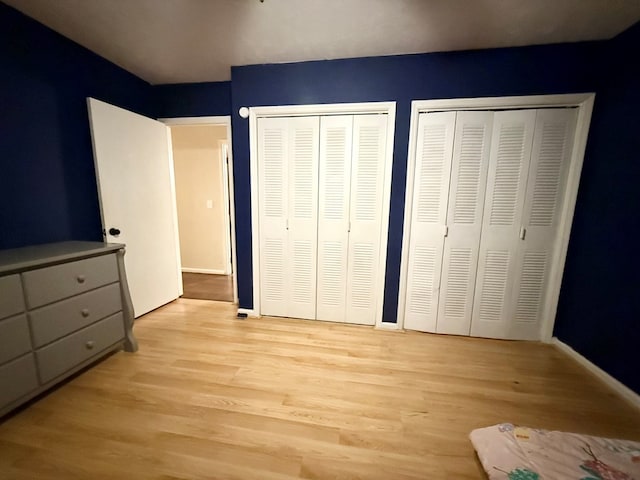 unfurnished bedroom with light wood finished floors, baseboards, and multiple closets