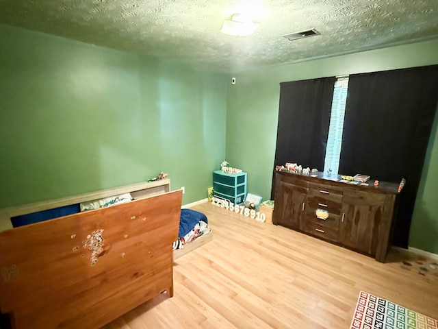 interior space with a textured ceiling, visible vents, wood finished floors, and baseboards