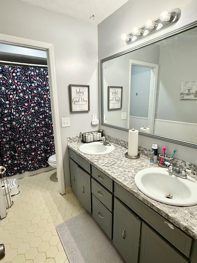 full bathroom featuring toilet, a textured ceiling, double vanity, and a sink