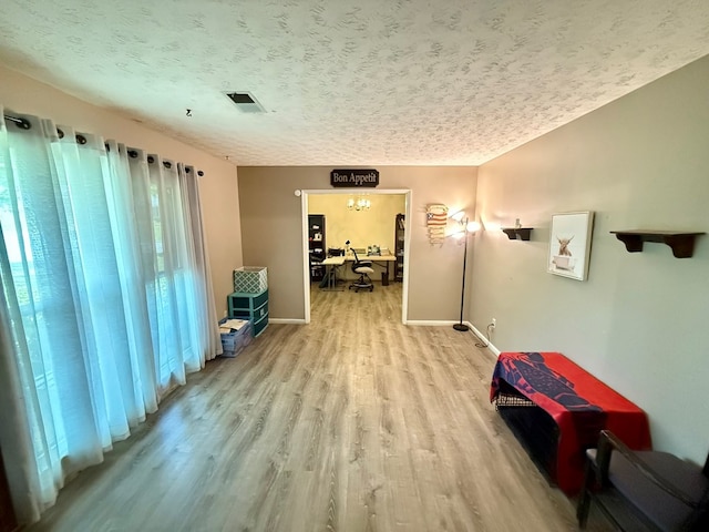 corridor featuring a textured ceiling, baseboards, visible vents, and wood finished floors