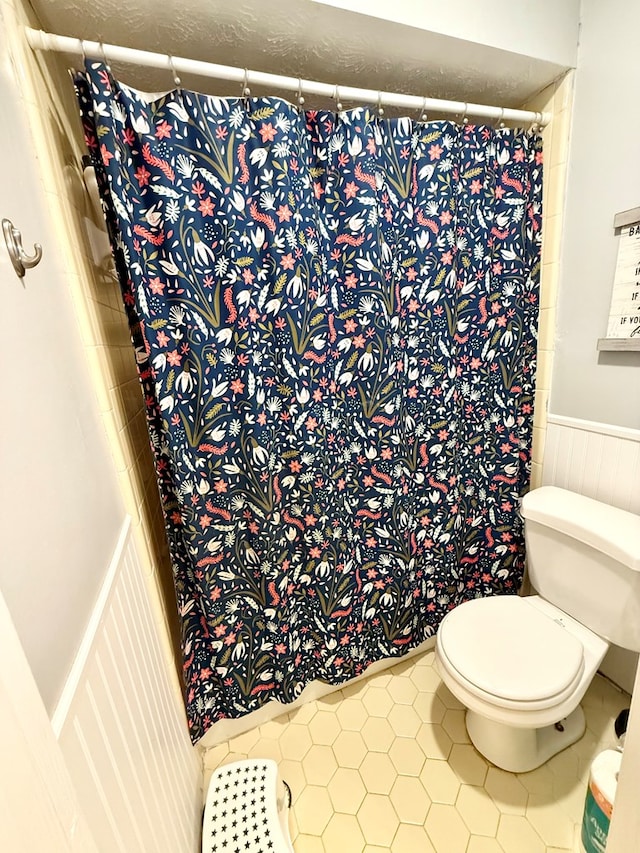 bathroom featuring curtained shower, toilet, a wainscoted wall, and tile patterned floors
