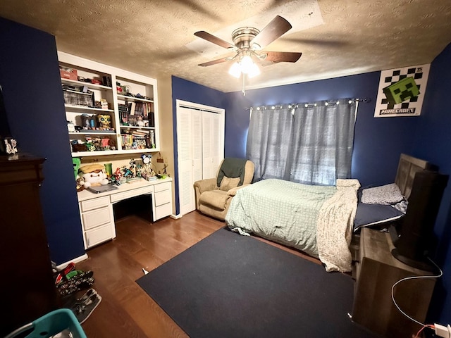 bedroom featuring built in desk, a closet, a textured ceiling, ceiling fan, and dark wood-style floors
