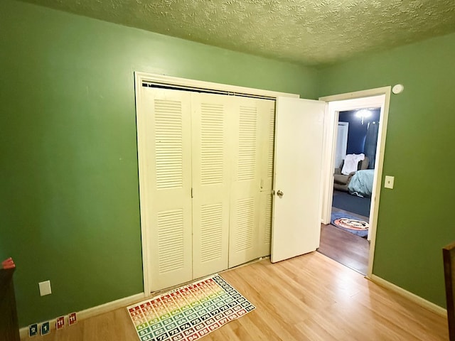 unfurnished bedroom with a closet, a textured ceiling, wood finished floors, and baseboards