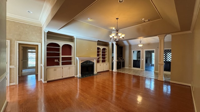 unfurnished living room with a high end fireplace, decorative columns, a tray ceiling, hardwood / wood-style flooring, and an inviting chandelier