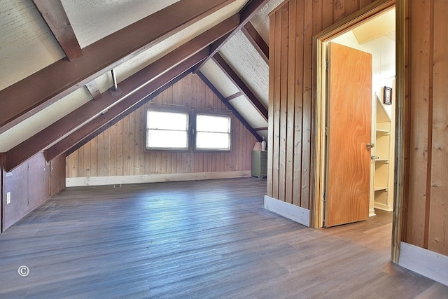 additional living space featuring wooden walls, hardwood / wood-style floors, and vaulted ceiling with beams