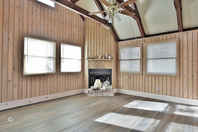 unfurnished living room with ceiling fan, hardwood / wood-style floors, wooden walls, a fireplace, and lofted ceiling with beams