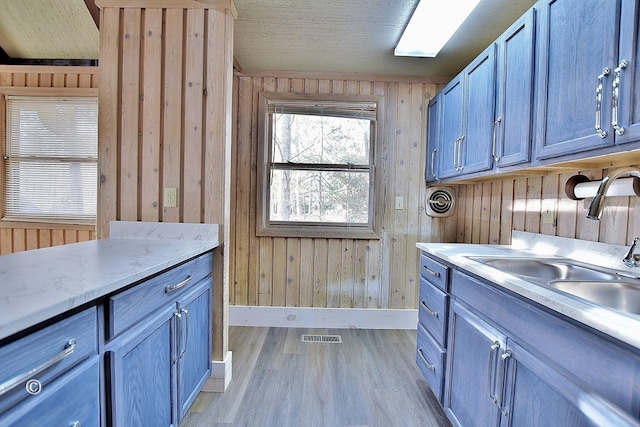 laundry area with wooden walls, sink, and light wood-type flooring