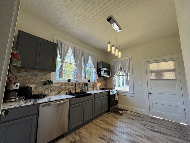 kitchen featuring decorative backsplash, stainless steel appliances, sink, light hardwood / wood-style floors, and hanging light fixtures