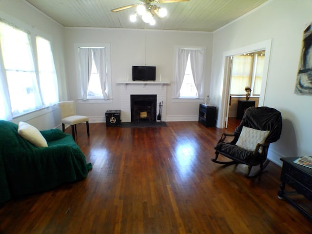 living room featuring wooden ceiling, dark wood-type flooring, crown molding, a brick fireplace, and ceiling fan