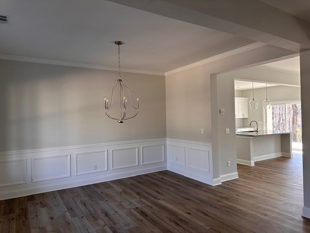 unfurnished dining area with dark wood-type flooring, visible vents, wainscoting, and ornamental molding