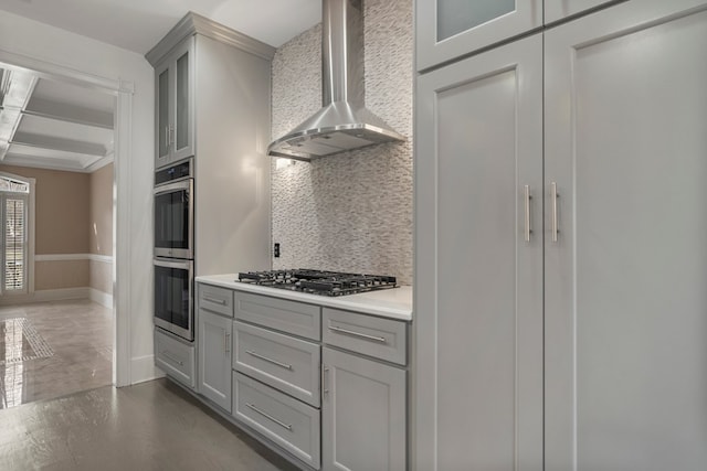 kitchen with appliances with stainless steel finishes, gray cabinetry, dark hardwood / wood-style flooring, wall chimney range hood, and backsplash