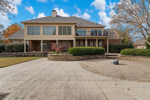 rear view of property featuring a balcony, a patio, and a lawn