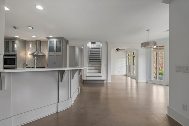 kitchen featuring crown molding, pendant lighting, sink, wall chimney range hood, and tasteful backsplash