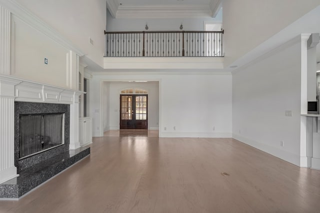 unfurnished living room featuring a high ceiling, a high end fireplace, french doors, and light hardwood / wood-style floors