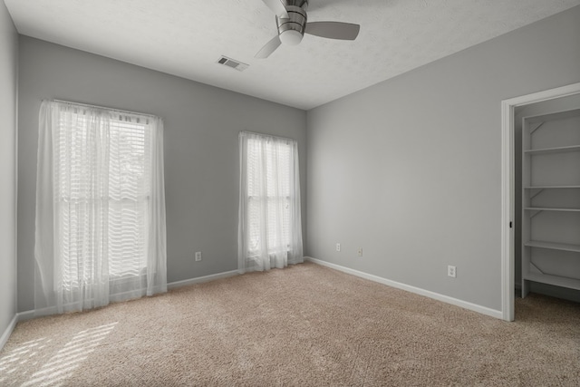 unfurnished bedroom featuring a walk in closet, ceiling fan, light carpet, and multiple windows