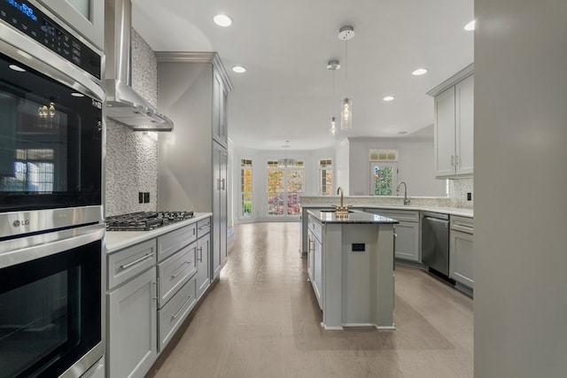 kitchen with pendant lighting, stainless steel appliances, wall chimney range hood, decorative backsplash, and gray cabinetry