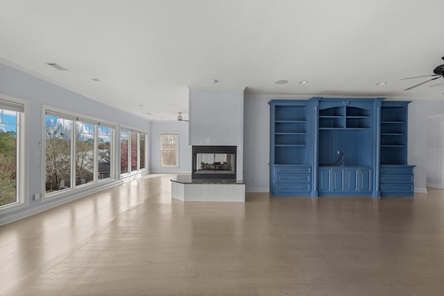 unfurnished living room featuring ceiling fan, light hardwood / wood-style flooring, a multi sided fireplace, and crown molding