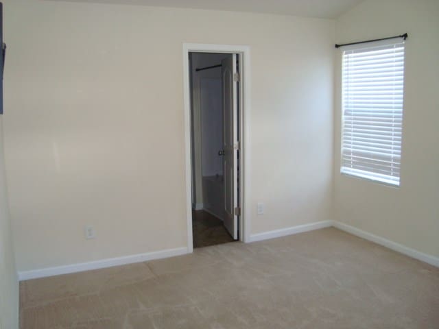 unfurnished bedroom with light colored carpet, a walk in closet, and vaulted ceiling