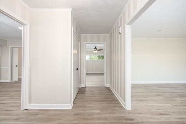 hall with light wood-type flooring, ornamental molding, and a textured ceiling