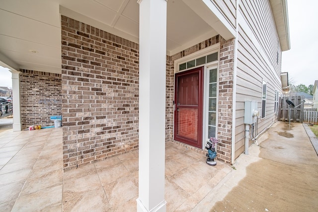 view of exterior entry featuring brick siding and fence