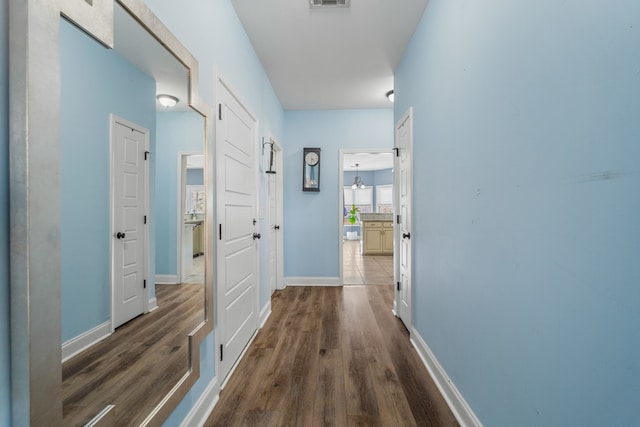 corridor with dark wood-style floors, visible vents, and baseboards