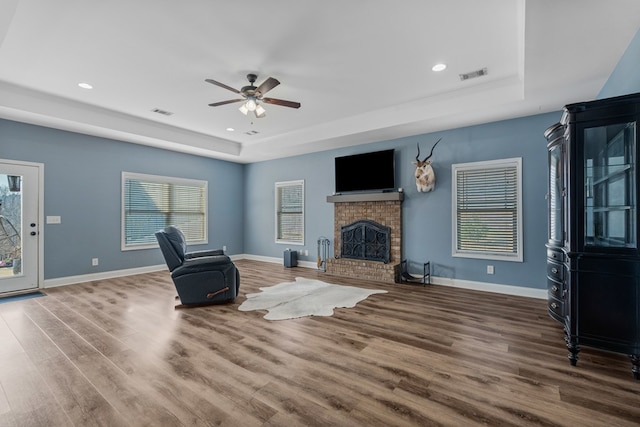 unfurnished living room featuring visible vents, a tray ceiling, wood finished floors, baseboards, and a brick fireplace