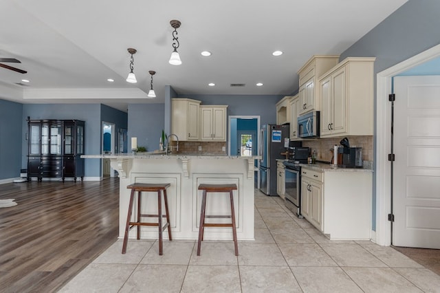 kitchen featuring light stone countertops, a peninsula, stainless steel appliances, cream cabinetry, and a kitchen breakfast bar