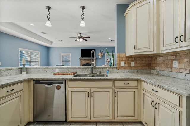 kitchen with a sink, stainless steel dishwasher, cream cabinets, light stone countertops, and hanging light fixtures