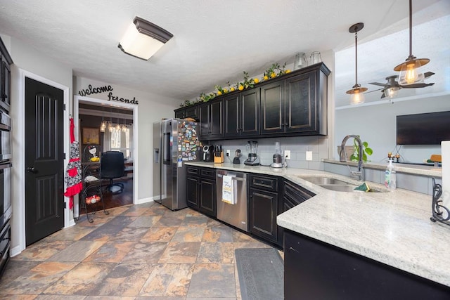 kitchen featuring dark cabinets, a sink, appliances with stainless steel finishes, stone finish floor, and pendant lighting