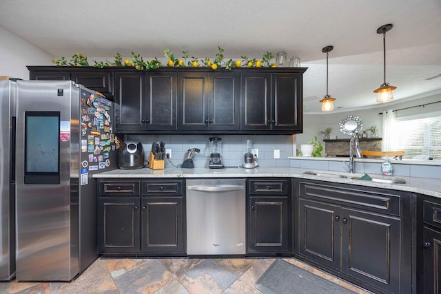 kitchen featuring light stone counters, decorative light fixtures, stainless steel appliances, backsplash, and a sink