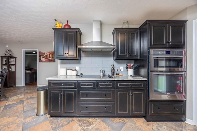 kitchen with black electric stovetop, wall chimney exhaust hood, tasteful backsplash, double oven, and baseboards