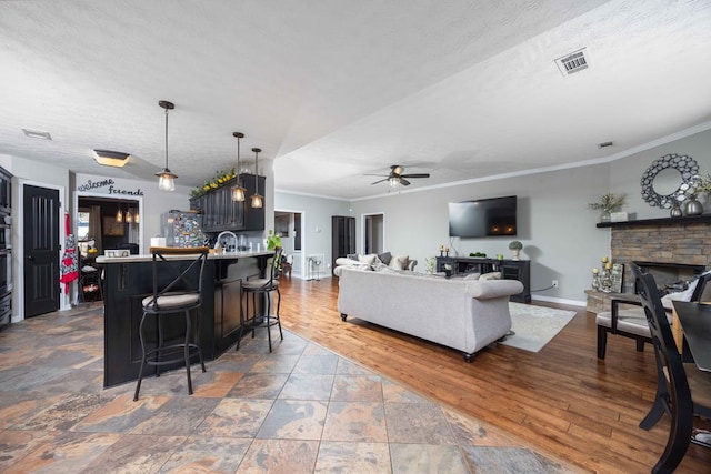 living room with baseboards, a ceiling fan, wood finished floors, crown molding, and a stone fireplace