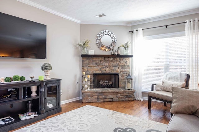 living room with visible vents, crown molding, a stone fireplace, and wood finished floors