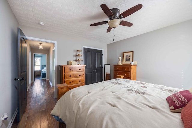 bedroom with a textured ceiling, dark wood-type flooring, a ceiling fan, baseboards, and a closet