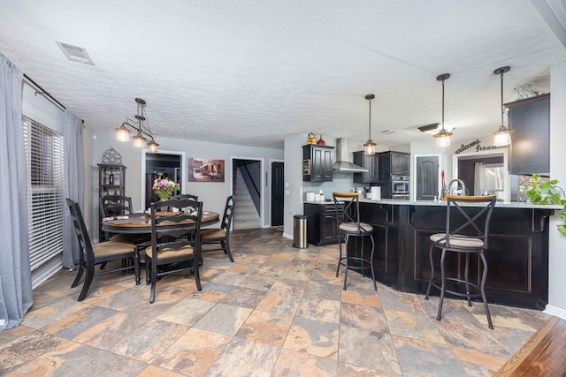 kitchen featuring stone finish flooring, visible vents, a kitchen breakfast bar, light countertops, and wall chimney exhaust hood