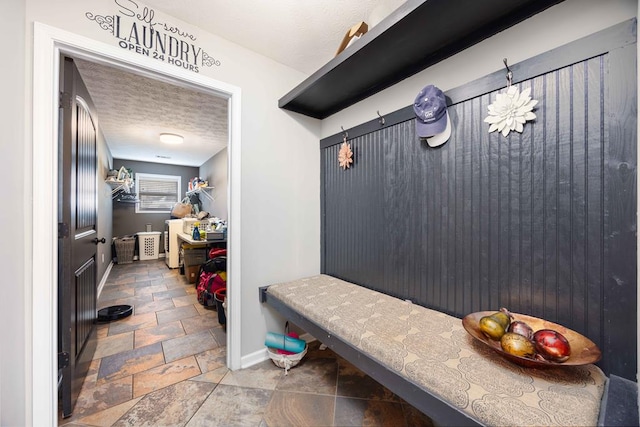 mudroom with stone finish floor, a textured ceiling, and baseboards