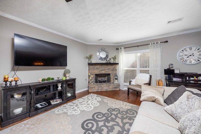 living room featuring a fireplace, visible vents, ornamental molding, a textured ceiling, and wood finished floors