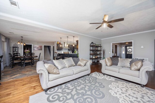 living area featuring visible vents, crown molding, light wood-style flooring, and ceiling fan