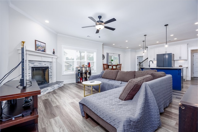 living room with ceiling fan, sink, ornamental molding, a fireplace, and light wood-type flooring