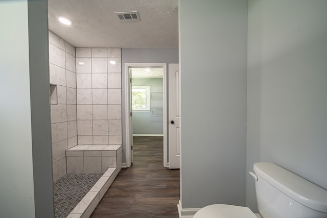 bathroom featuring tiled shower, wood-type flooring, a textured ceiling, and toilet