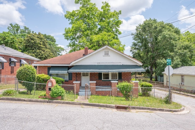 bungalow-style house with a fenced front yard, brick siding, a gate, a chimney, and covered porch