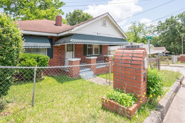bungalow-style house featuring brick siding, a fenced front yard, a front yard, and a chimney