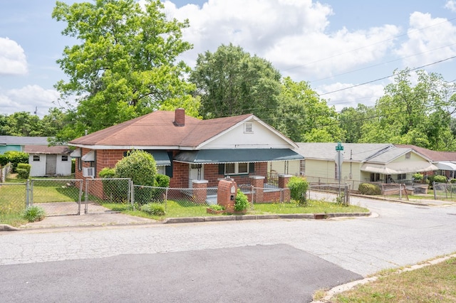 view of front of property featuring a porch, a fenced front yard, a chimney, a gate, and brick siding
