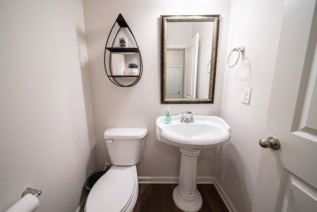 half bath with toilet, baseboards, and wood finished floors