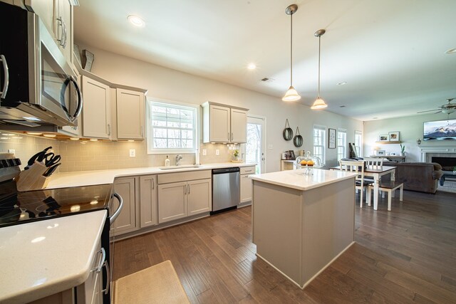 kitchen featuring tasteful backsplash, a kitchen island, a sink, dark wood-style floors, and appliances with stainless steel finishes