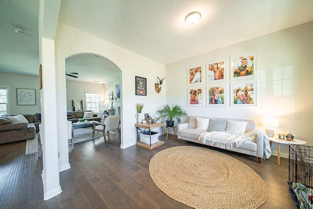 living area with arched walkways, dark wood-style flooring, and baseboards