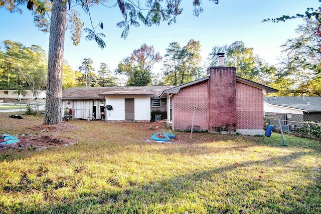 rear view of property featuring brick siding, a lawn, a chimney, and fence