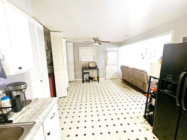 kitchen with ceiling fan, black fridge with ice dispenser, white cabinetry, light countertops, and light floors