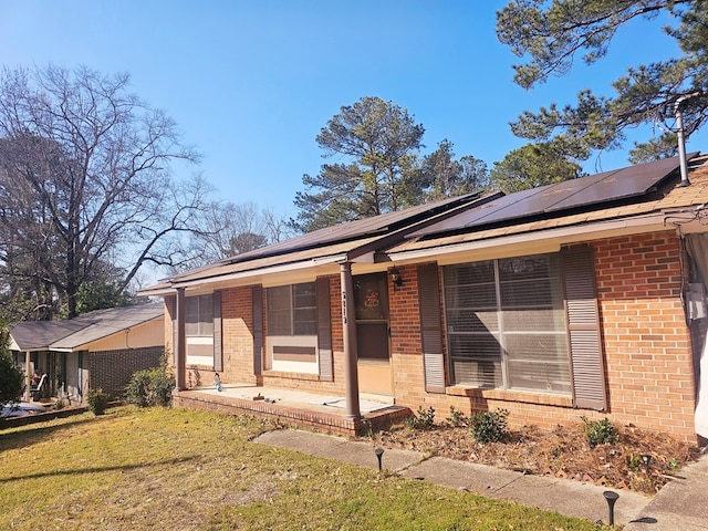 ranch-style home with brick siding, a porch, a front yard, and roof mounted solar panels