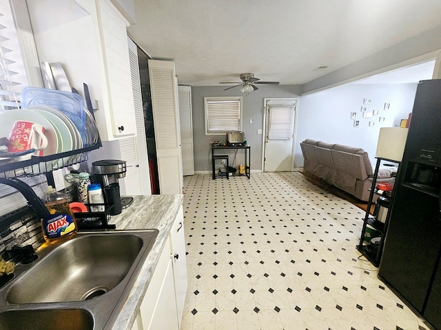 kitchen with a sink, white cabinetry, baseboards, a ceiling fan, and light countertops